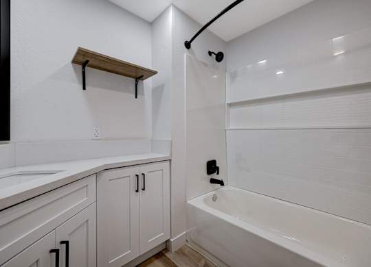 A white bathroom with a tub, sink, and shelving.