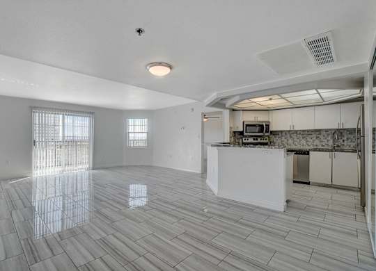 A spacious kitchen and living room with white tiled floors and a large window.
