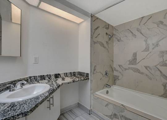 A bathroom with a marble patterned shower and a white sink.