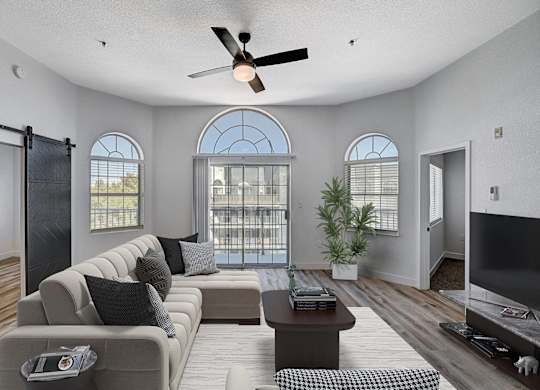 A living room with a grey sofa, a coffee table, a ceiling fan, and a sliding glass door.
