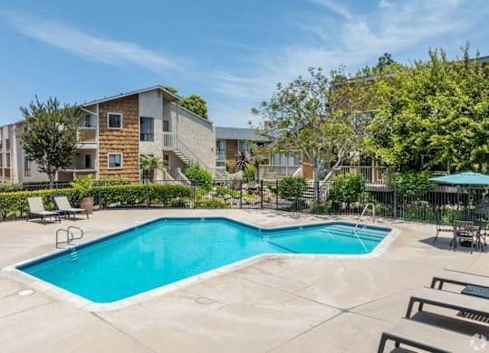 A swimming pool surrounded by lounge chairs and trees in a residential area.