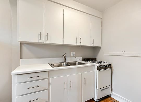A white kitchen with a sink, stove, and cabinets.