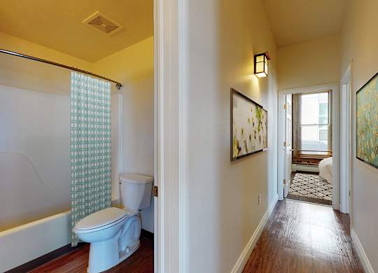 A bathroom with a toilet, a bathtub, and a window with a curtain.