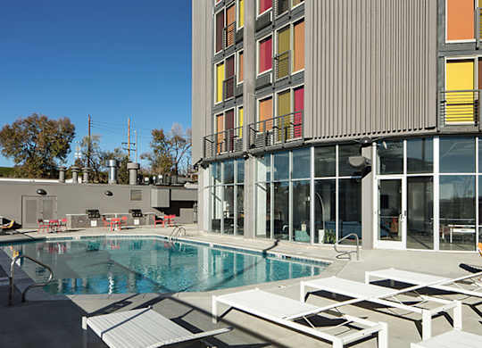 A swimming pool is surrounded by sun loungers in front of a modern building.