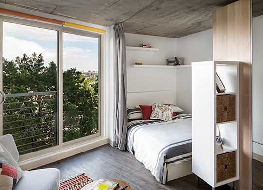 A bedroom with a bed, a chair, and a window with a view of trees.