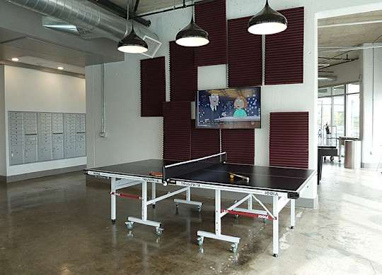 A ping pong table is in the middle of a room with a TV on the wall.