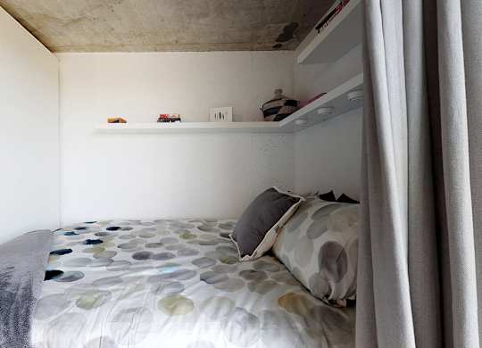 A bed with a grey and white patterned comforter and a grey pillow is in the foreground of the image.