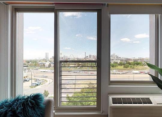 A view of a cityscape through a window with a blue cushion on the left and a plant on the right.