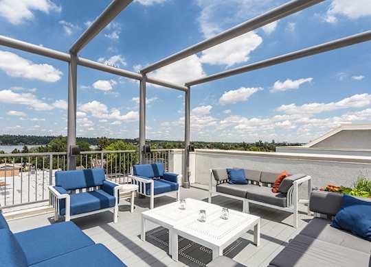 A white table with a glass top sits on a patio with blue cushions.