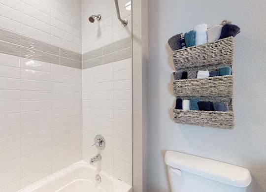 A white bathtub with a shower head and a basket of towels on the wall.