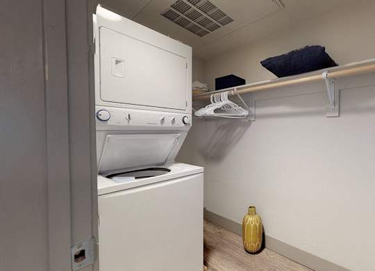 A yellow vase sits on the floor next to a white oven and dryer.