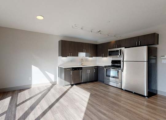 A modern kitchen with stainless steel appliances and wooden flooring.