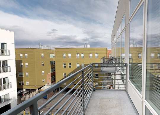 A balcony with a metal railing and glass windows overlooks a courtyard with a metal staircase.