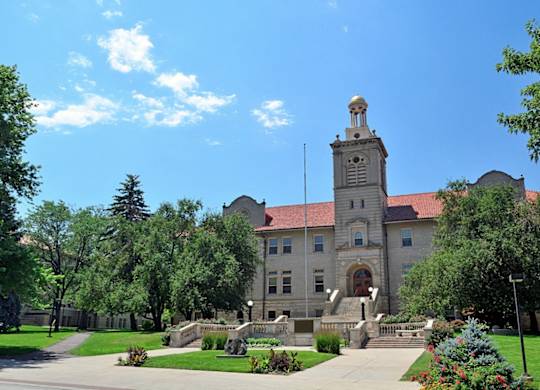 A large building with a tower and a red roof is surrounded by trees and greenery.