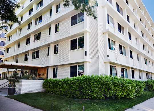 A white building with a green hedge in front.