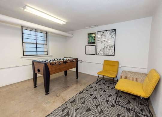 A room with a foosball table, two chairs, and a bench.