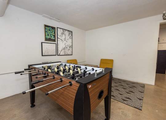 A foosball table sits in a room with a rug and two framed pictures on the wall.