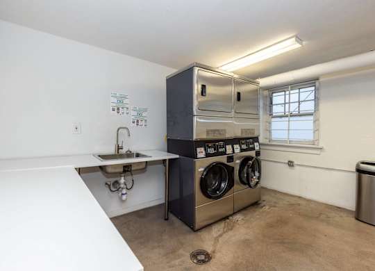 A laundry room with a washer and dryer, sink, and trash can.