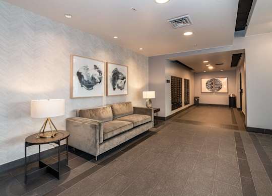 A living room with a grey sofa and a table with a lamp on it.