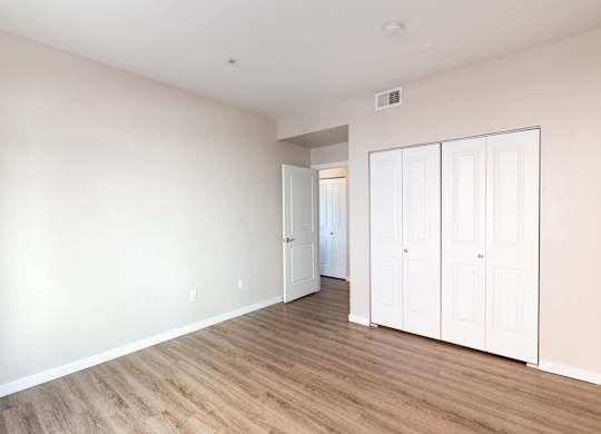 A room with white walls and wooden flooring with a white door on the right.
