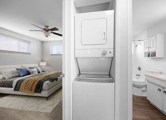 A white fridge is in the middle of a room with a bed and a bathroom.