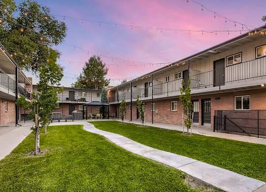 A sunset view of apartment buildings with a green lawn in the foreground.