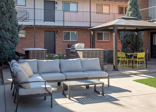 A patio with a white couch, yellow chairs, and a table with a tree in a pot.