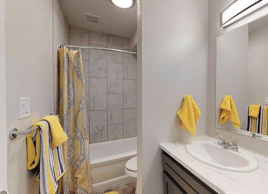 A bathroom with a white sink, a striped towel, and a yellow towel.