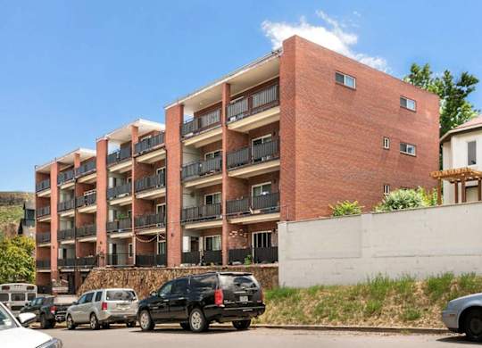 A red brick building with balconies and cars parked in front.