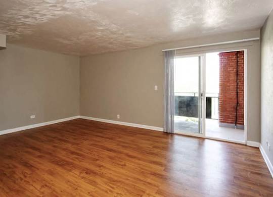A room with wooden floors and a sliding glass door leading to a balcony.