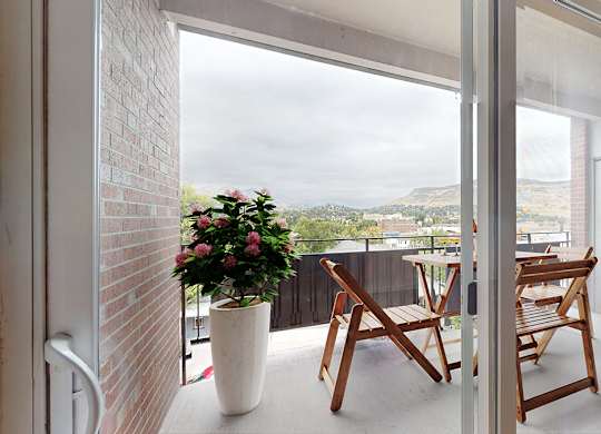 A white vase with pink flowers sits on a patio next to two wooden chairs.