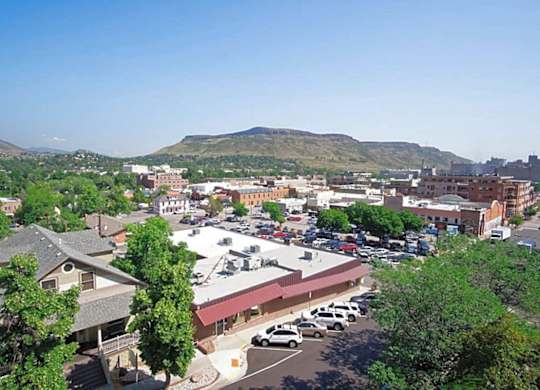 A parking lot with cars and a building in the foreground with trees and mountains in the background.