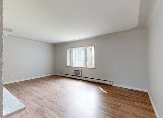 A room with wooden flooring and a window with blinds.