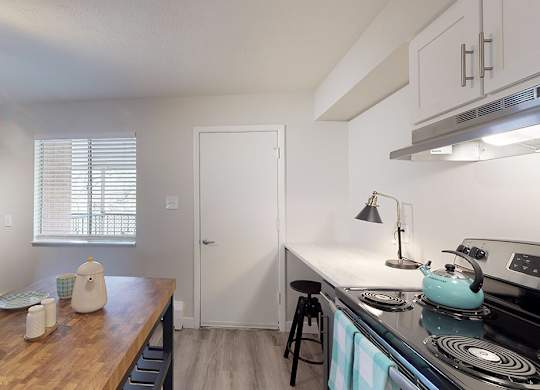 A kitchen with a stove, refrigerator, and a counter with plates and cups on it.