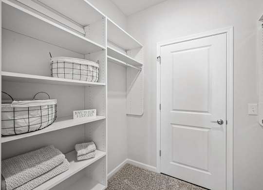 A white closet with a basket on the shelf and towels on the shelf.