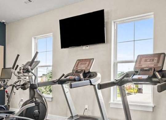 A treadmill with a TV mounted on the wall above it.