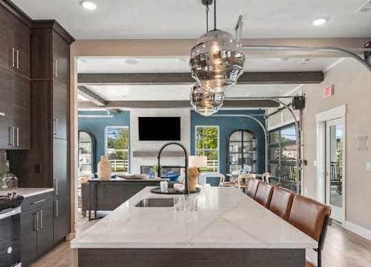 A modern kitchen with a long island and brown chairs.