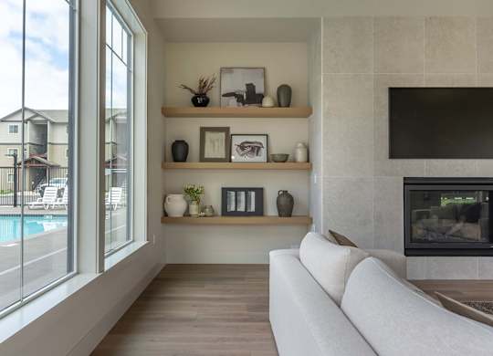 A modern living room with a fireplace and a large window overlooking a pool at Marcola Apartment Homes, Forest Grove