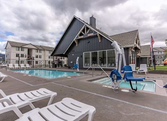 A large outdoor swimming pool with lounge chairs and a building in the background at Marcola Apartment Homes, Oregon