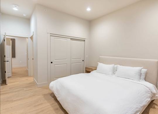 A white bed with a white headboard and two white pillows in a bedroom with wooden floors and white walls at Westgate Apartment Homes, Pendleton, Oregon
