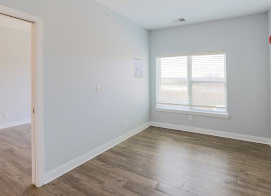 A room with a wooden floor and a window with blinds.