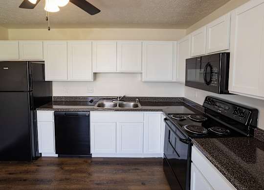 A black refrigerator is in a kitchen with white cabinets.