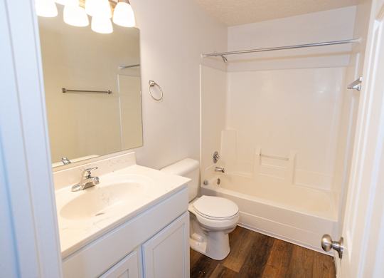 A white bathroom with a toilet, sink, mirror, and shower.