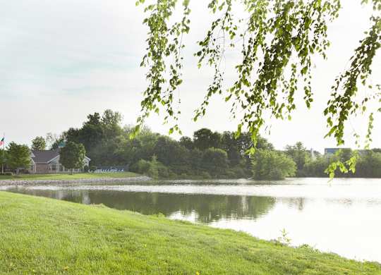 A serene lake surrounded by lush greenery and a house in the distance.