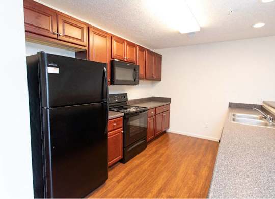 A black refrigerator is in a kitchen with wooden cabinets and a microwave.