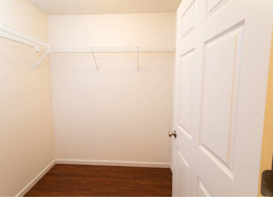 A white door is on the right side of a room with a white wall and a white closet rod.