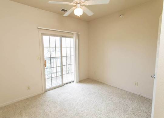 A room with a ceiling fan and a sliding glass door.