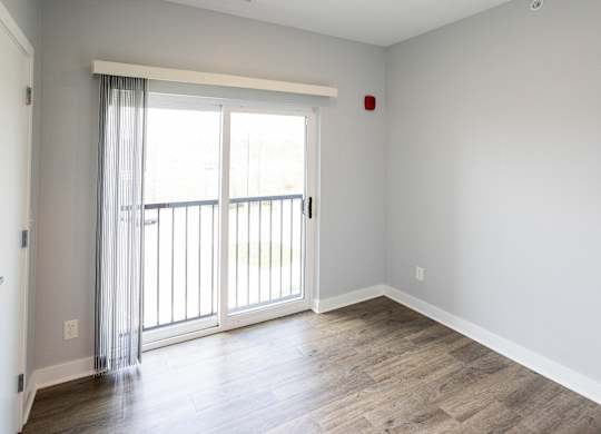 A room with a sliding glass door and wooden flooring.