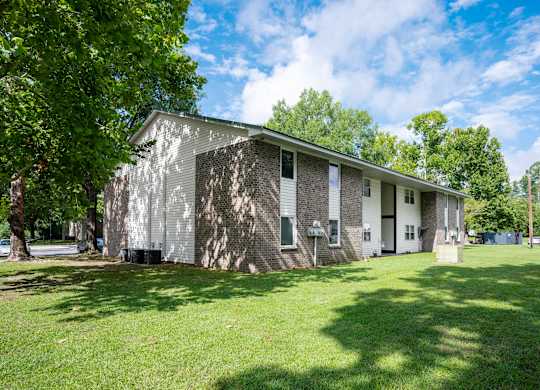 A house with a grey and white exterior is surrounded by a grassy lawn and trees at Sawbranch Apartments, Summerville, SC, 29485