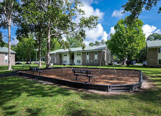 A playground with a slide and a swing set in a grassy area. at Sawbranch Apartments, Summerville 29485